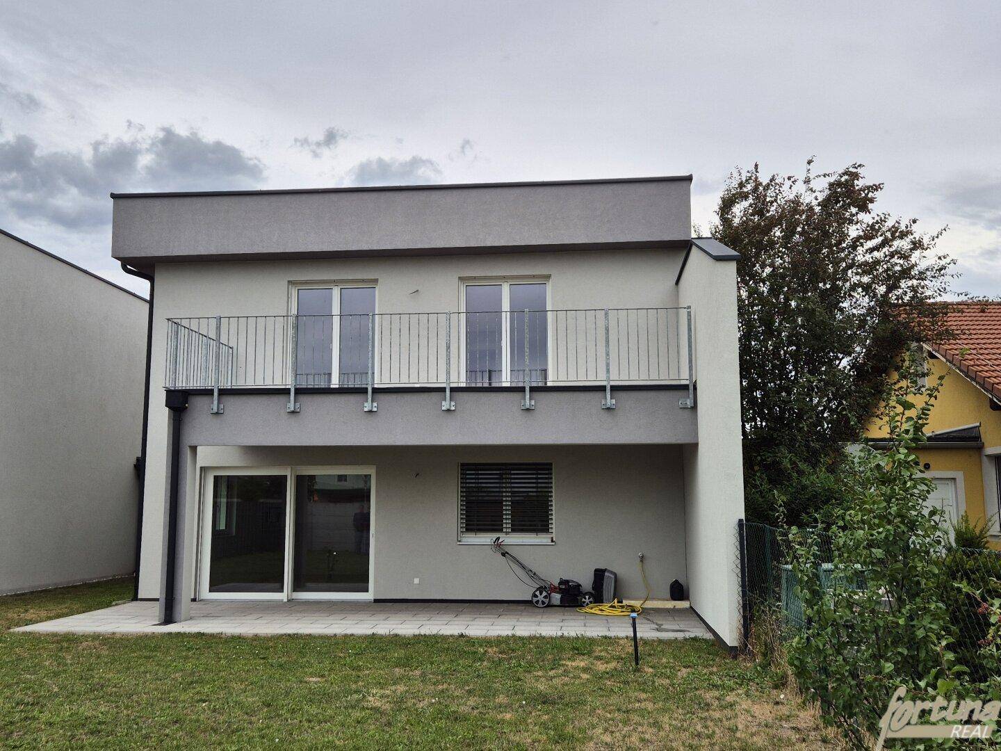 Rückansicht des modernen Hauses mit Balkon, Terrasse und angrenzendem Gartenbereich.
