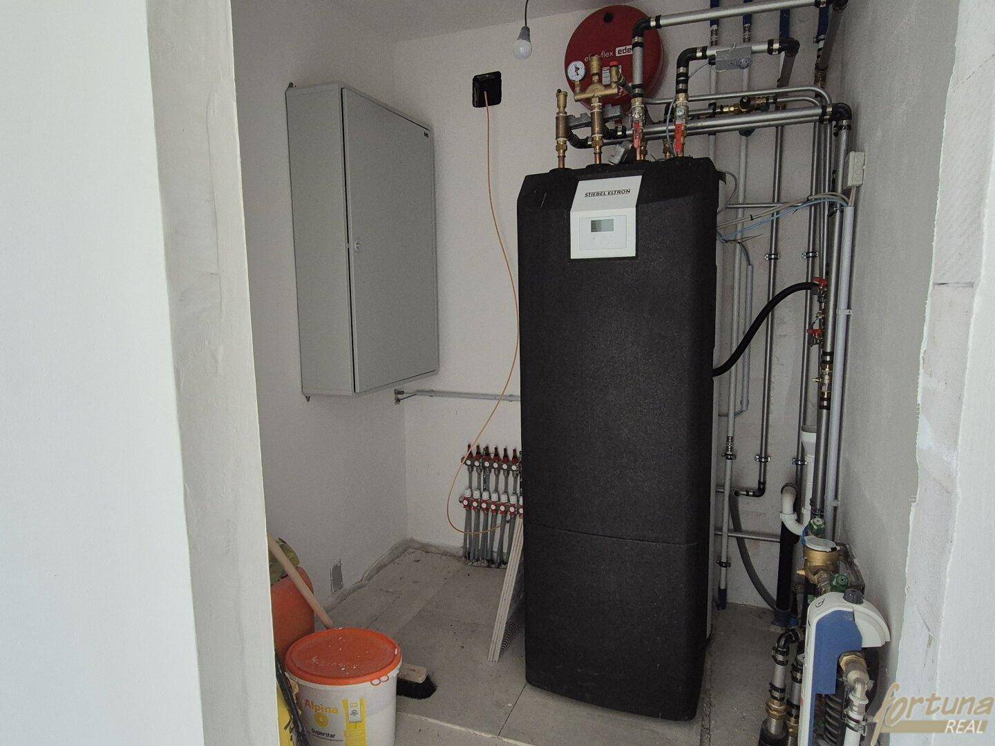 Technikraum mit moderner Heizungsanlage, Warmwasserspeicher und zahlreichen Rohrleitungen.