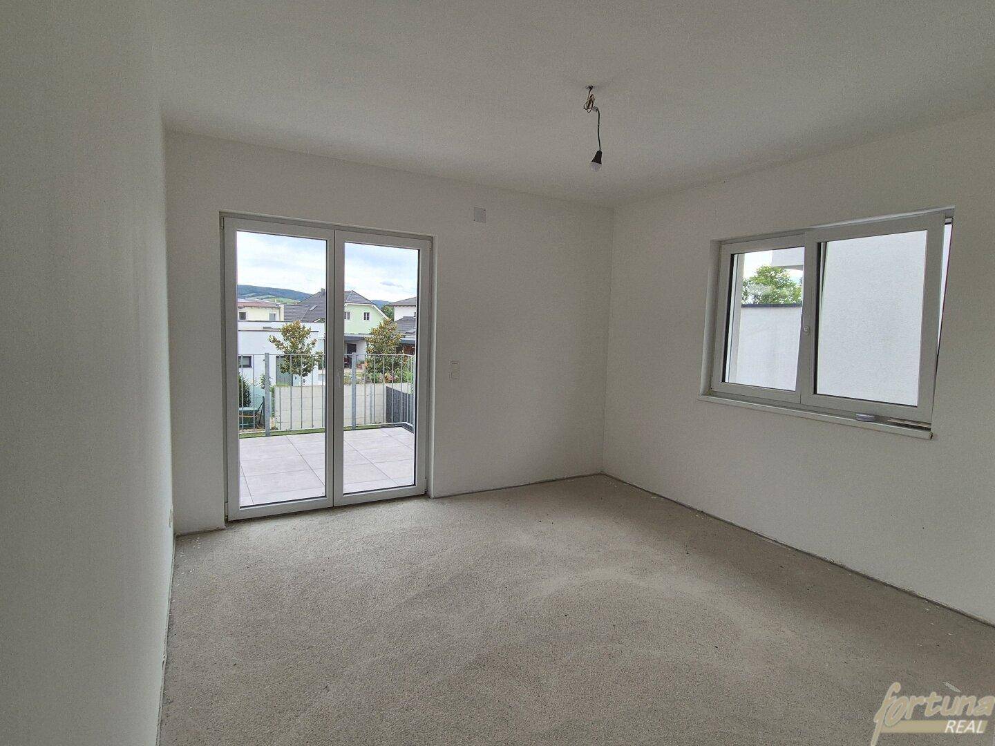 Heller Raum im Rohbauzustand mit großer Schiebetür zum Außenbereich und Fenster.