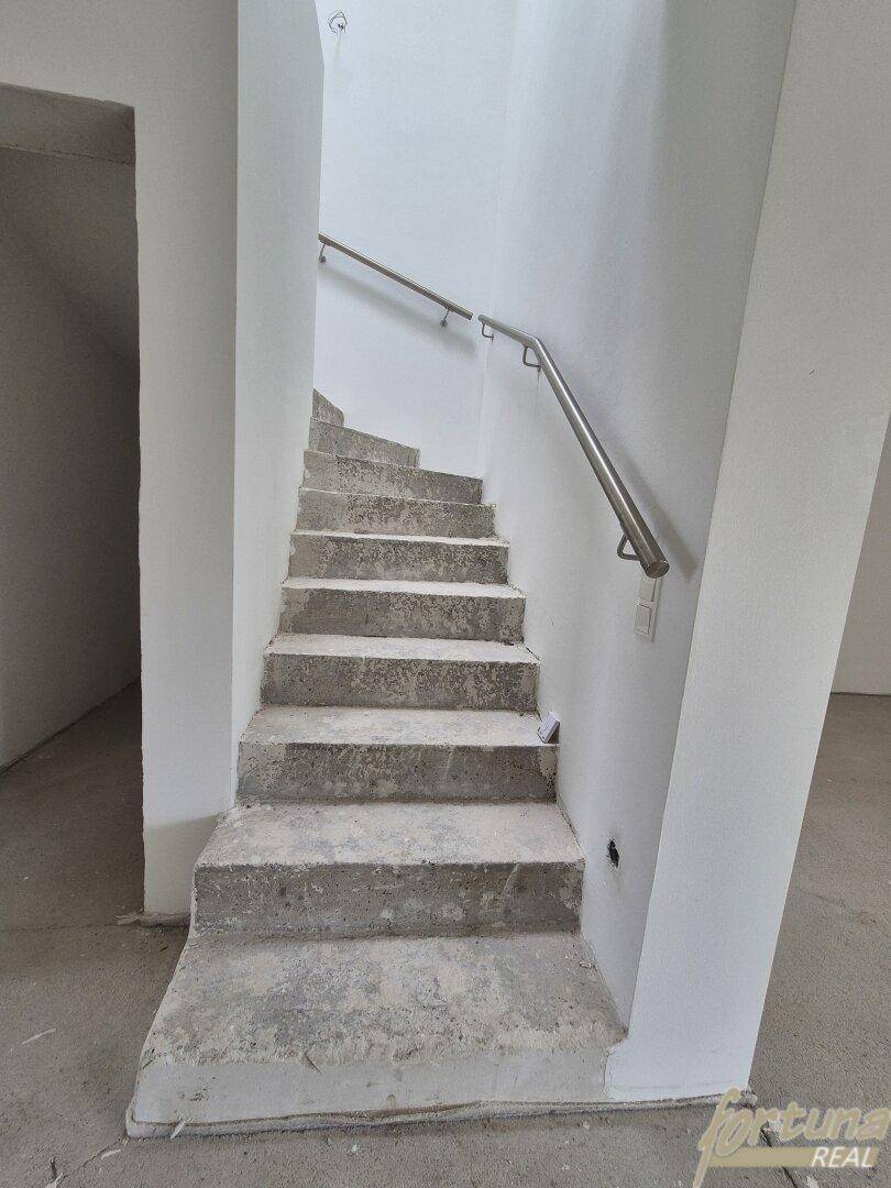 Unfertige Betontreppe mit einfachem Metallhandlauf in einem Rohbauzustand.
