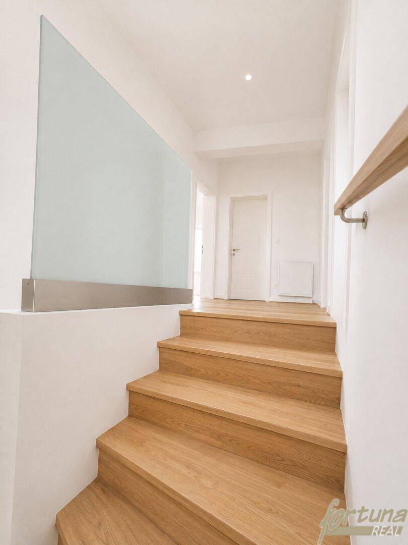 Moderne Holztreppe mit elegantem Glasgeländer und hellem, freundlichem Flur.