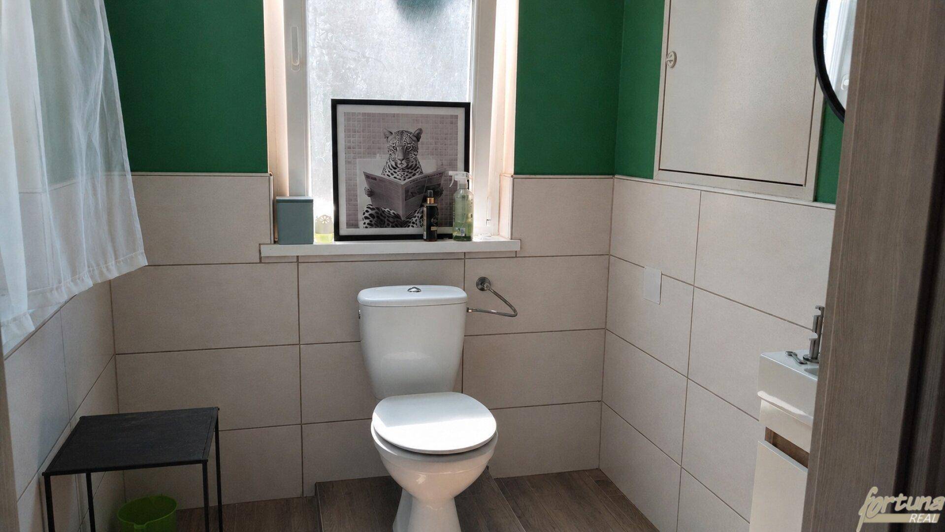 Modernes Gäste-WC mit grünen Wänden, beigen Fliesen und einem Fenster für Tageslicht.