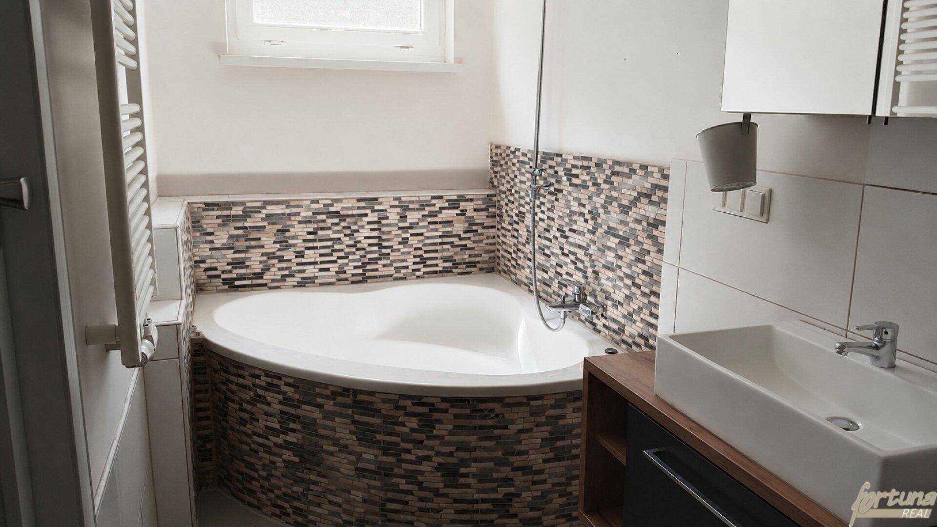 Badezimmer mit einer Eckbadewanne, Mosaikfliesen und einem modernen Waschbecken.