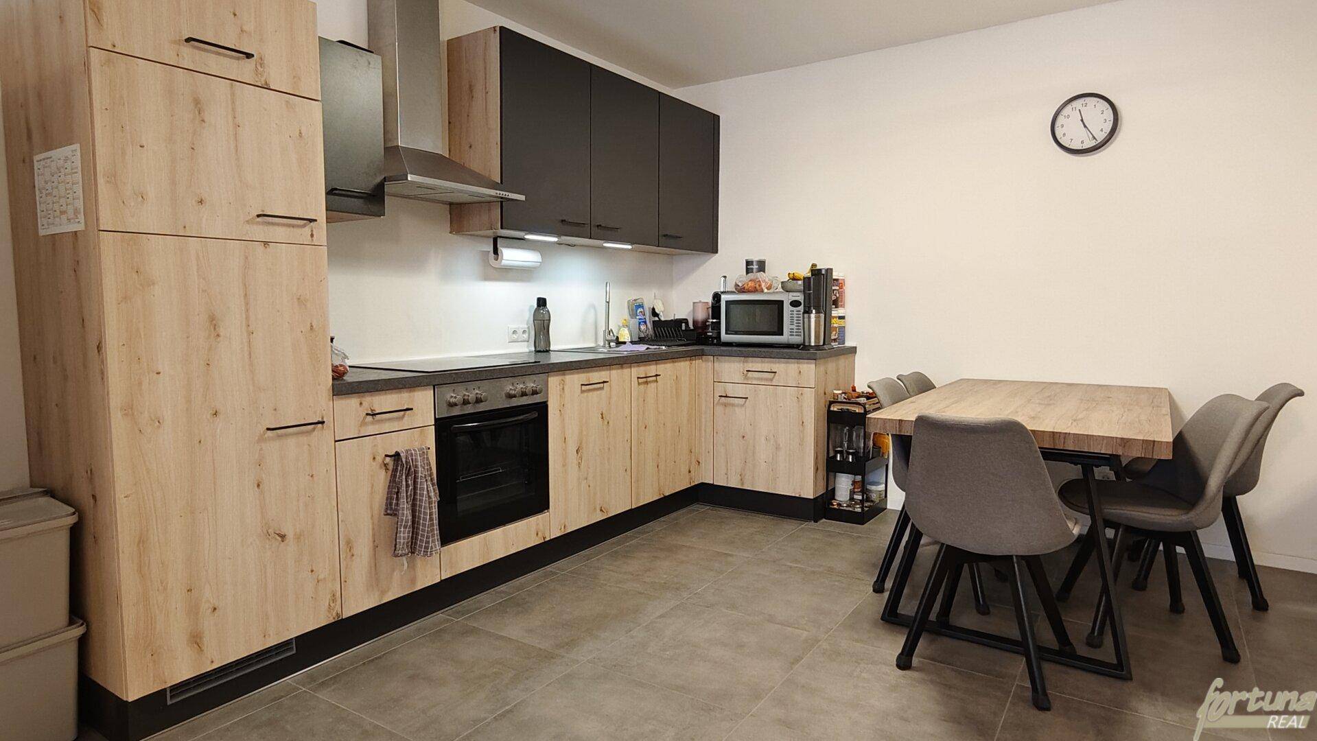 Funktionale Küche mit hellen Holzschränken, dunkler Arbeitsplatte und Essplatz für mehrere Personen.
