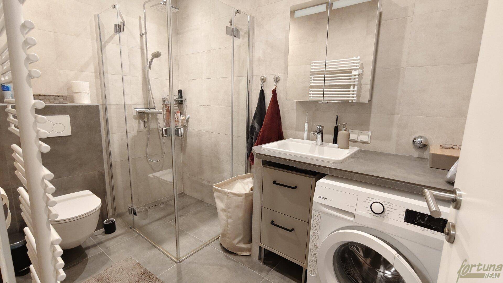 Modernes Badezimmer mit ebenerdiger Dusche, Waschbecken und integrierter Waschmaschine, sehr praktisch.