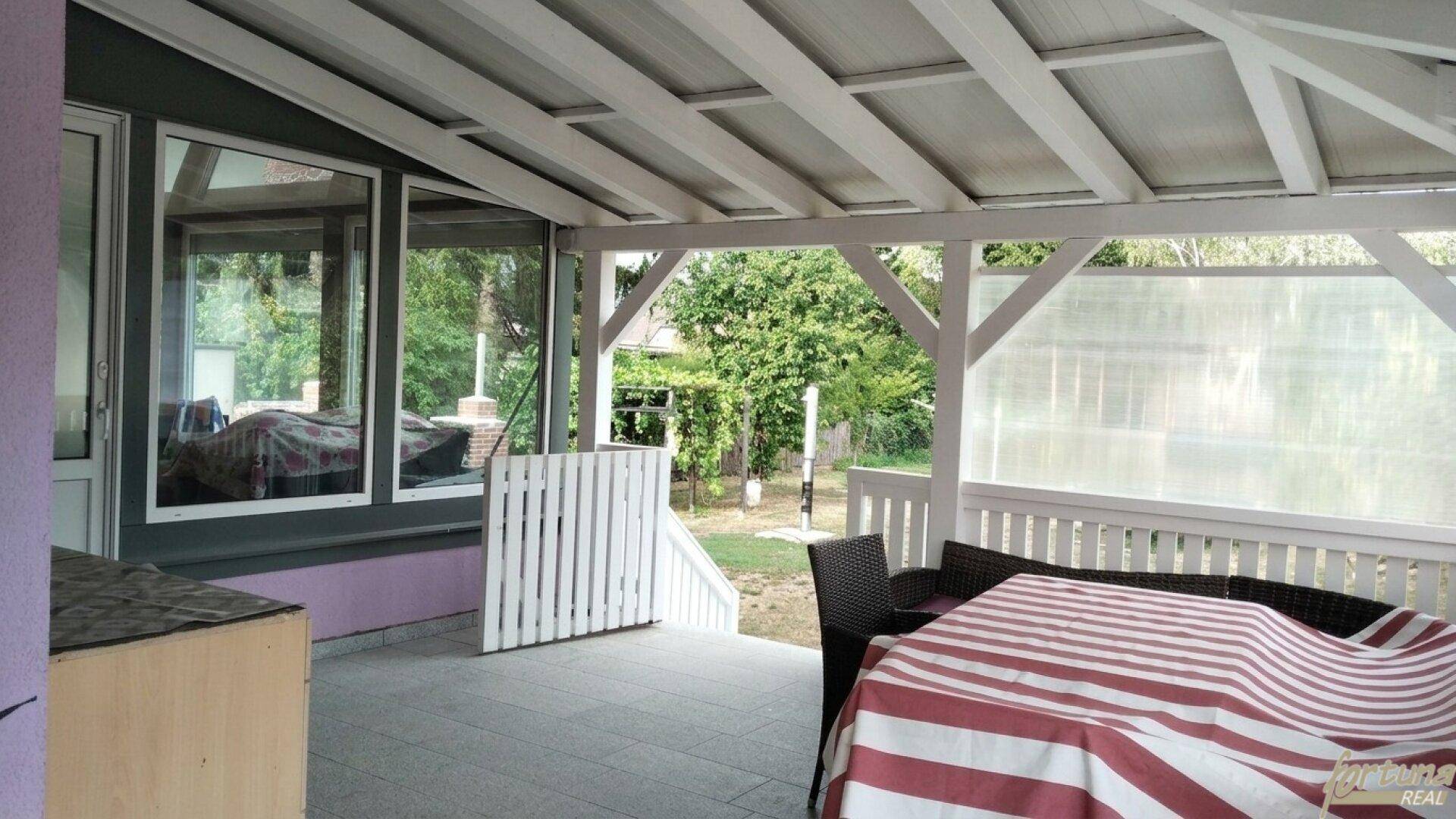 Geräumige überdachte Terrasse mit Gartenmöbeln und Fliesenboden, ideal für Mahlzeiten im Freien.