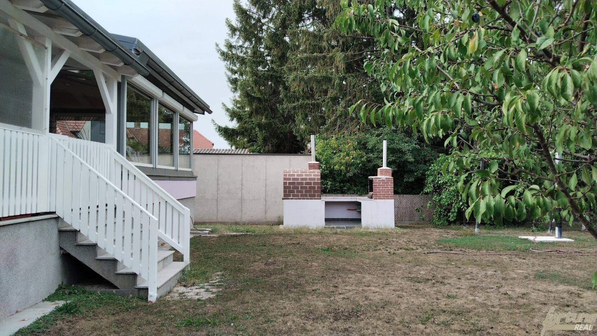 Gartenbereich mit gemauertem Grillplatz und altem Baumbestand, ideal für sommerliche Zusammenkünfte.