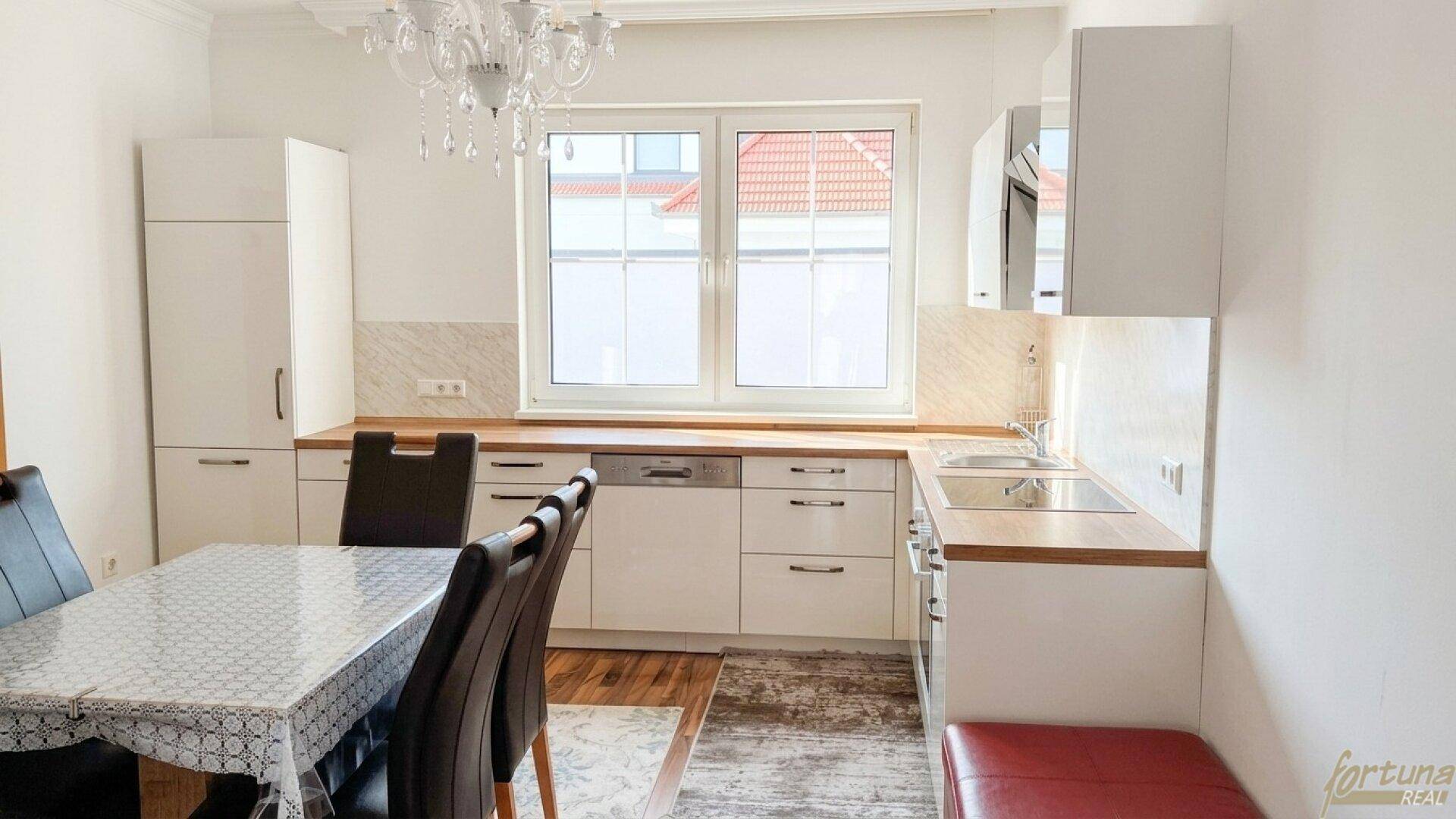 Moderne weiße Küche mit Holzarbeitsplatten und Essbereich, ausgestattet mit Geschirrspüler und Fenster.