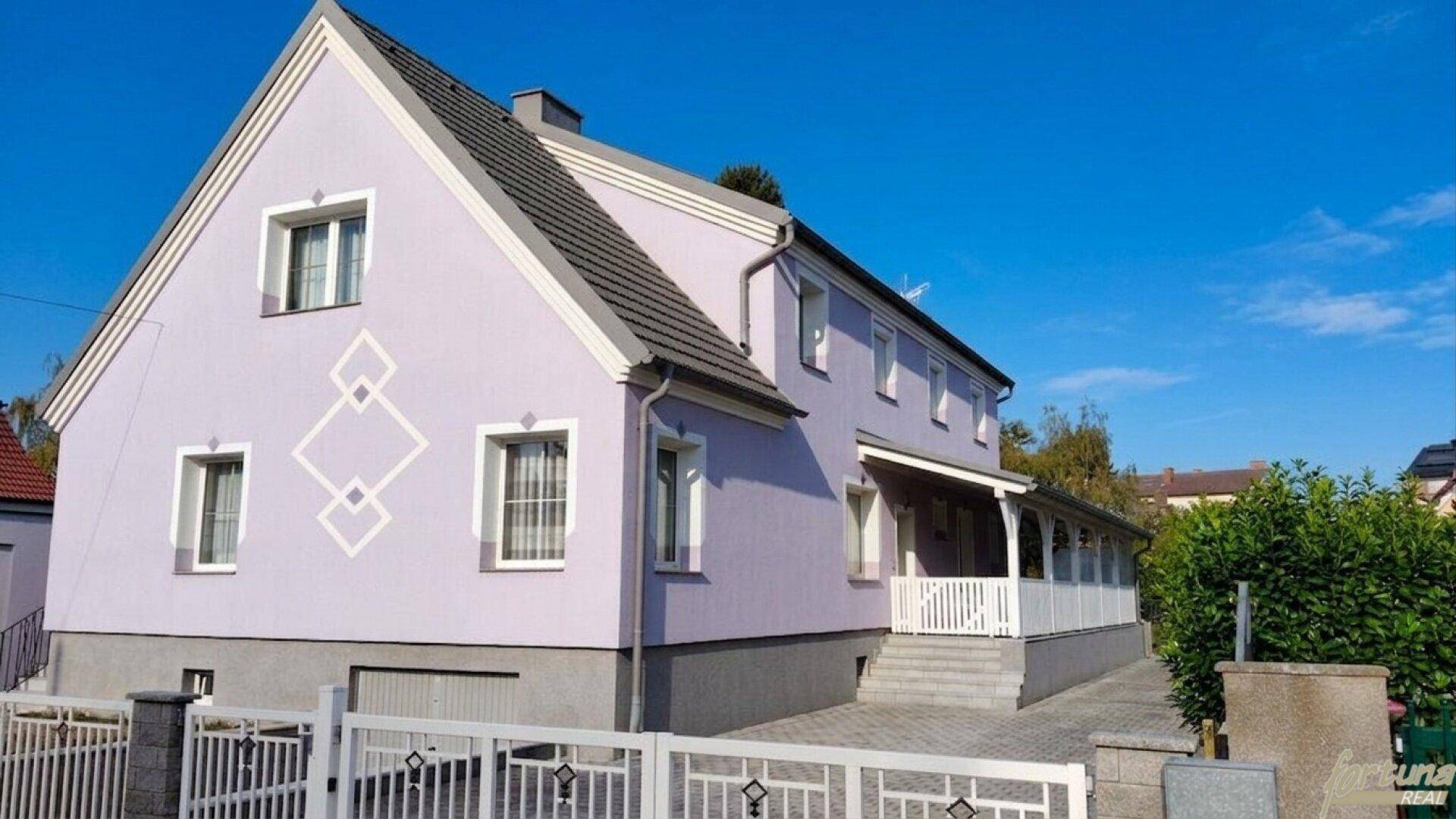 Seitenansicht des Hauses mit violetter Fassade, dekorativen Elementen und gepflasterter Einfahrt.