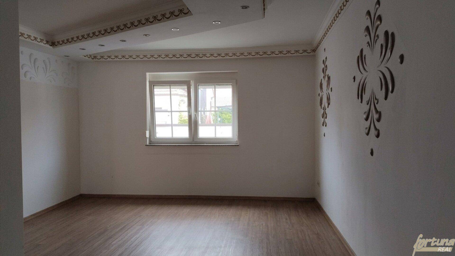 Leerer Raum mit hellem Laminatboden und dekorativen Wand- und Deckenverzierungen, bereit zur Einrichtung.