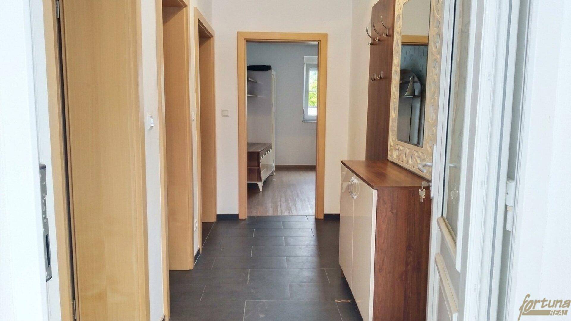 Heller Flur mit dunklem Fliesenboden, Holztüren und einem Spiegel, der zu weiteren Räumen führt.