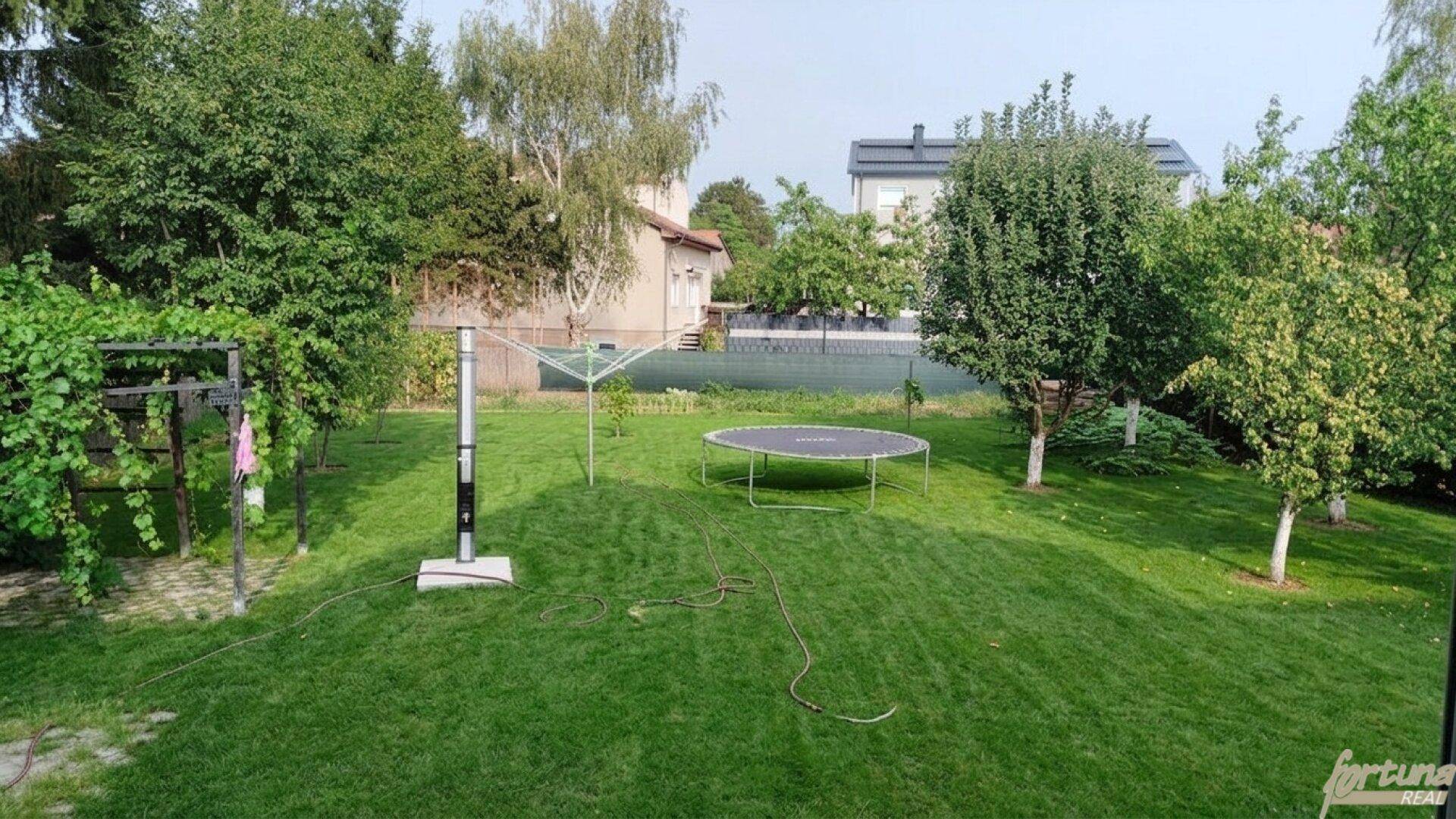 Großer, gepflegter Garten mit Rasenfläche, Trampolin und Wäscheleine, umgeben von Bäumen.