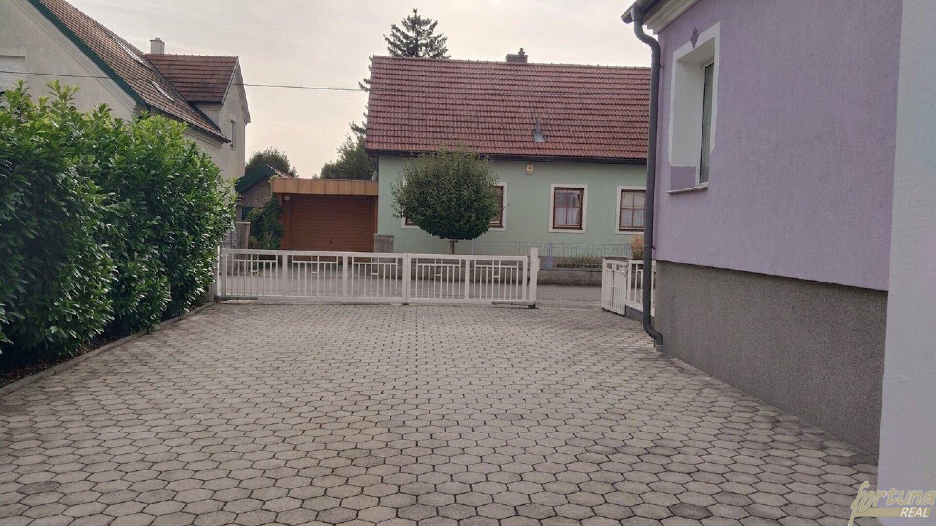 Gepflasterte Einfahrt mit weißem Tor und Zugang zum Haus, umgeben von einer ruhigen Wohngegend.