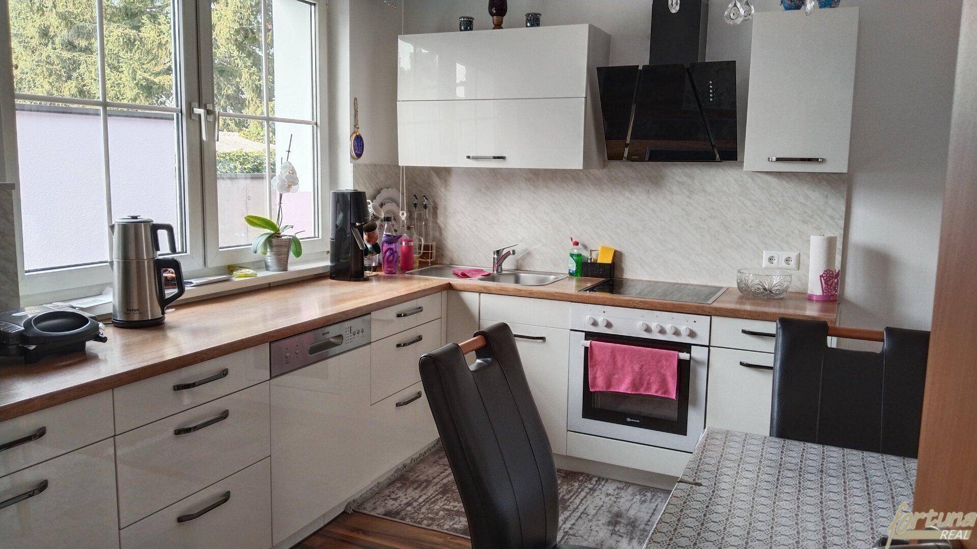 Moderne Küche mit weißen Hochglanzfronten, Holzarbeitsplatte und Blick ins Grüne durch das Fenster.