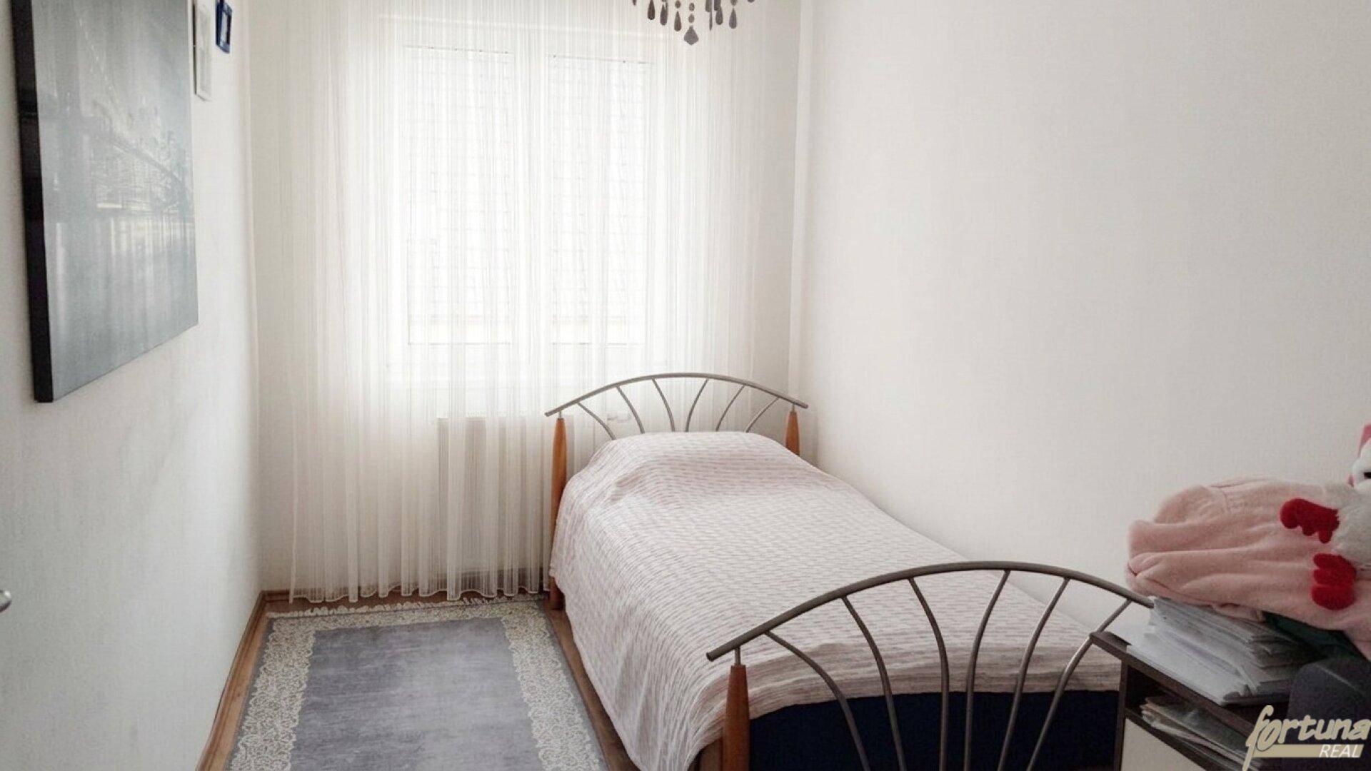 Kleines Schlafzimmer mit Einzelbett, hellem Fenster und schlichtem Teppich.