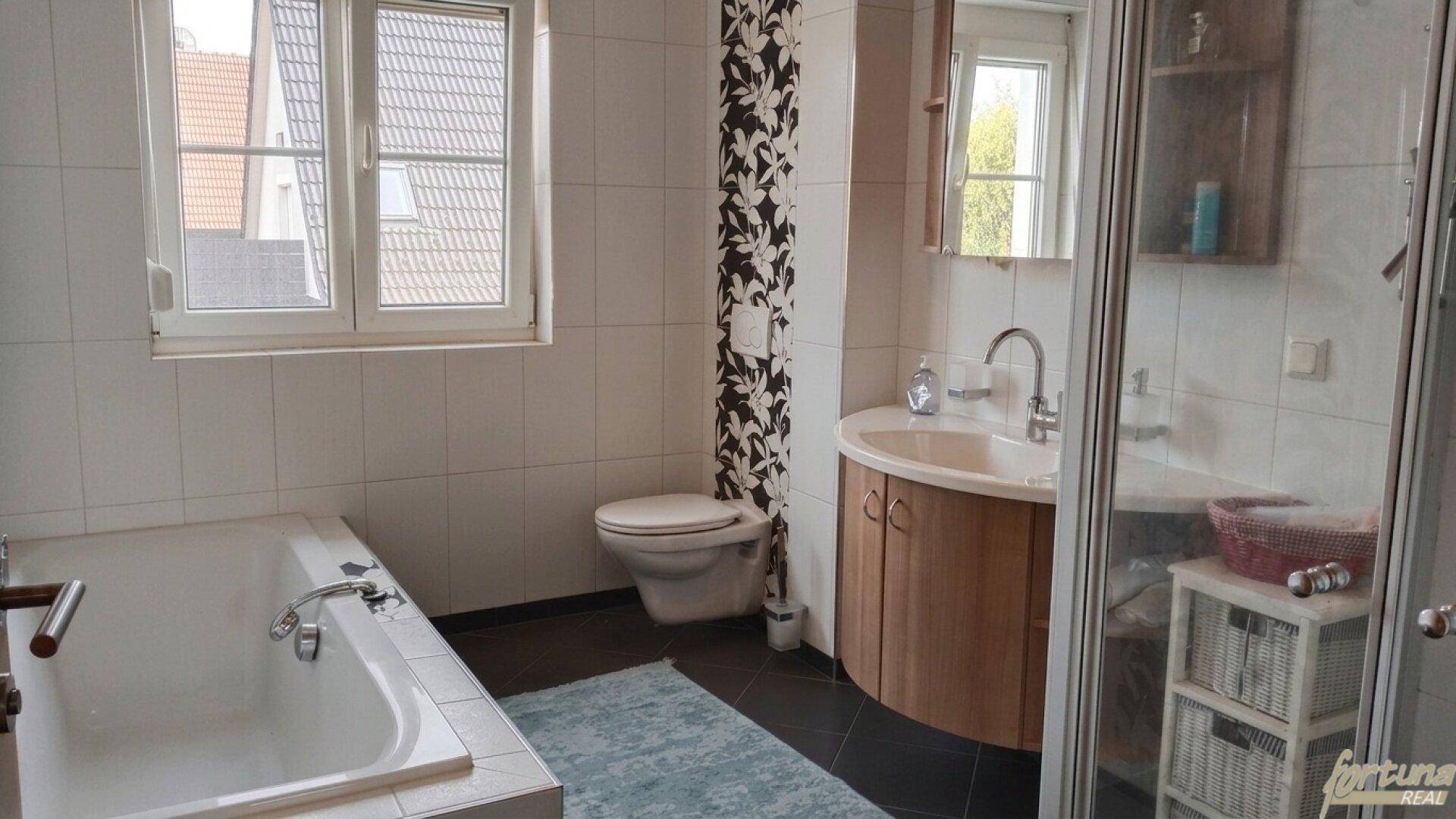 Helles Badezimmer mit Badewanne, Dusche, Waschbecken und Fenster.