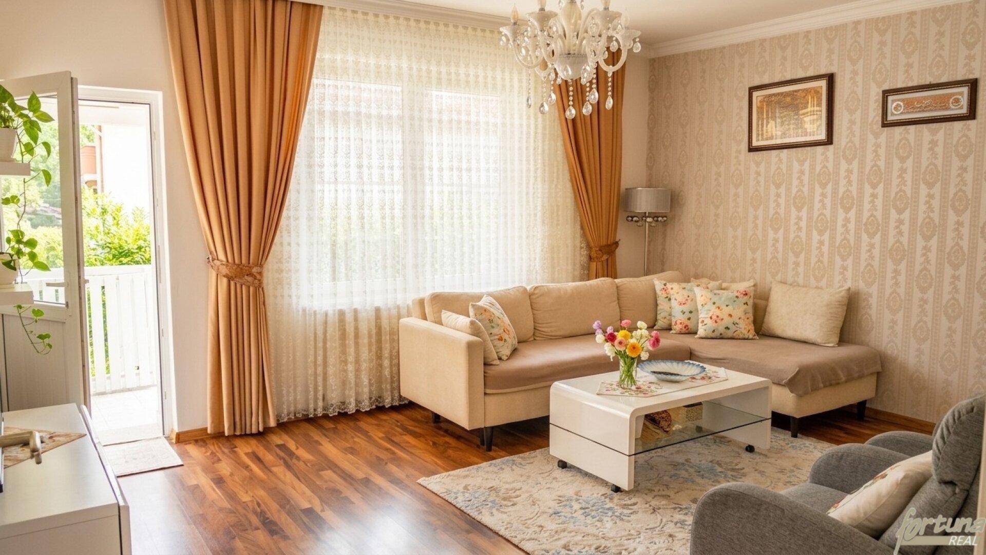 Helles Wohnzimmer mit großem Fenster, Vorhängen und Zugang zu einem Balkon, gemütlich eingerichtet.