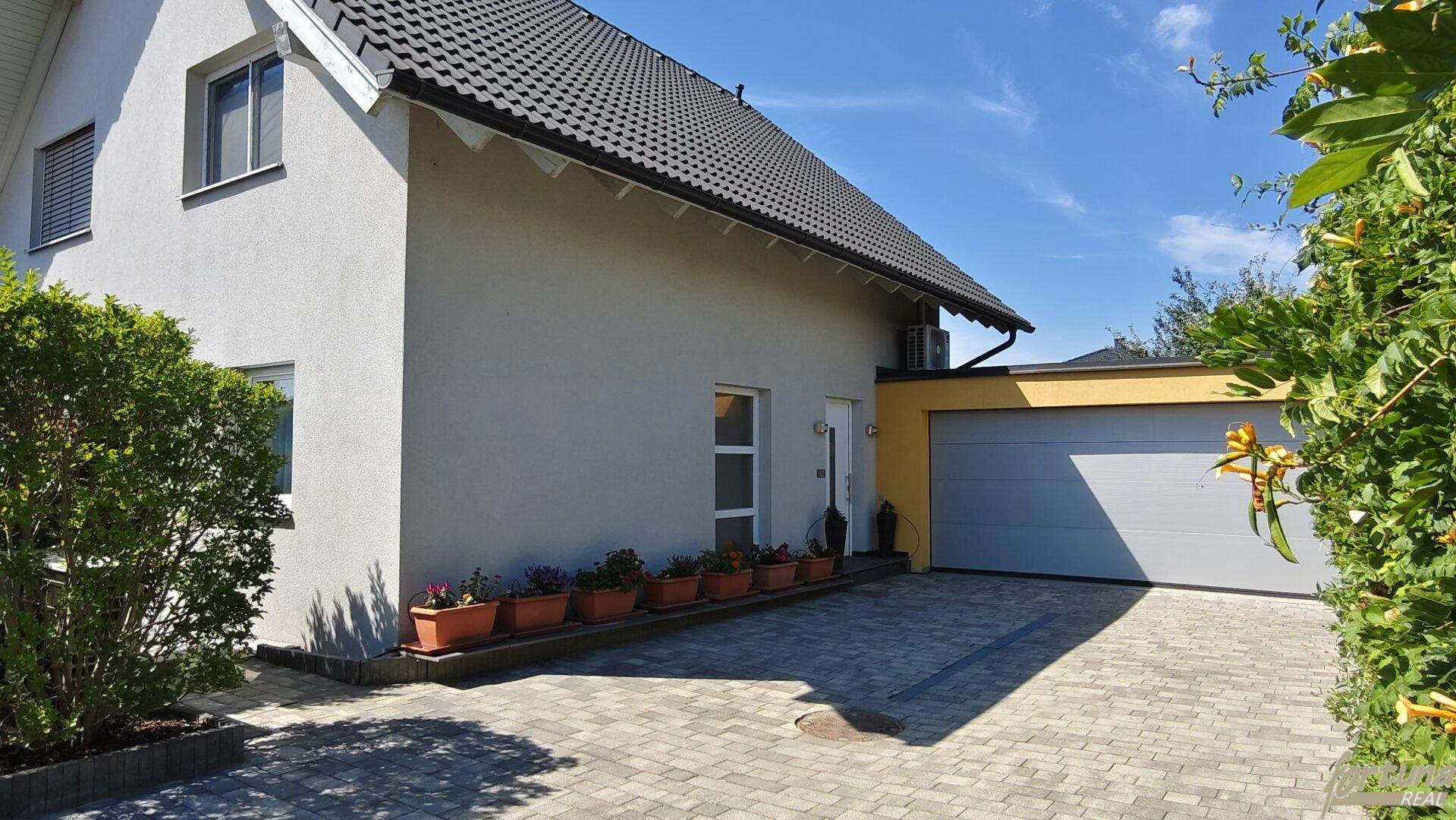 Seitenansicht des Hauses mit integrierter Garage und gepflasterter Zufahrt.