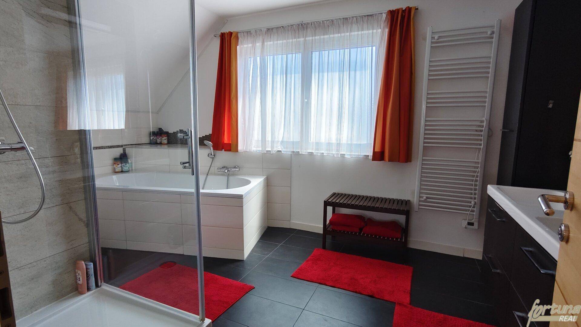 Geräumiges Badezimmer mit Badewanne, Dusche, beheiztem Handtuchhalter und Fenster.