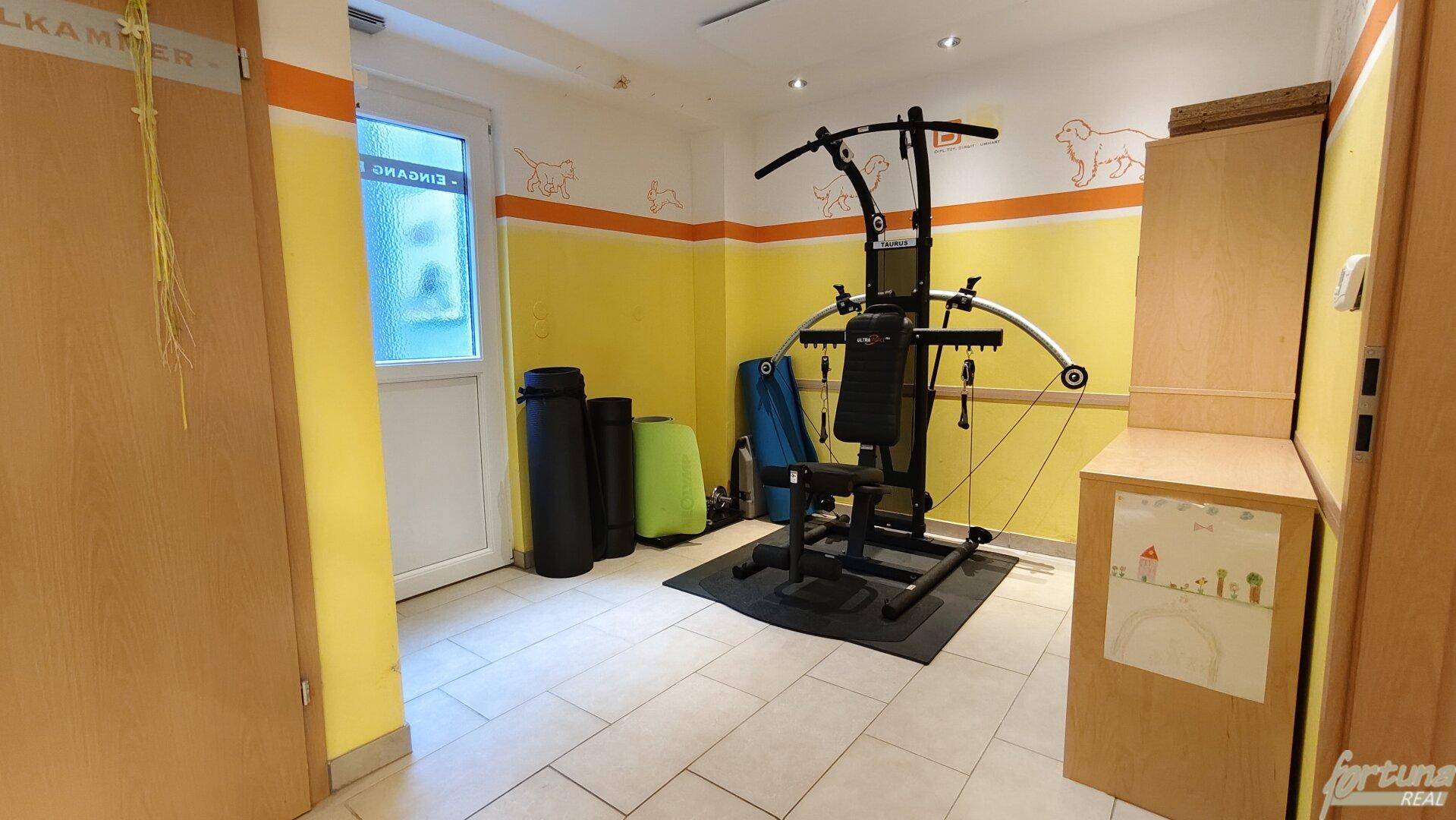 Fitnessraum mit Trainingsgeräten, Fliesenboden und farbenfroher Wandgestaltung.