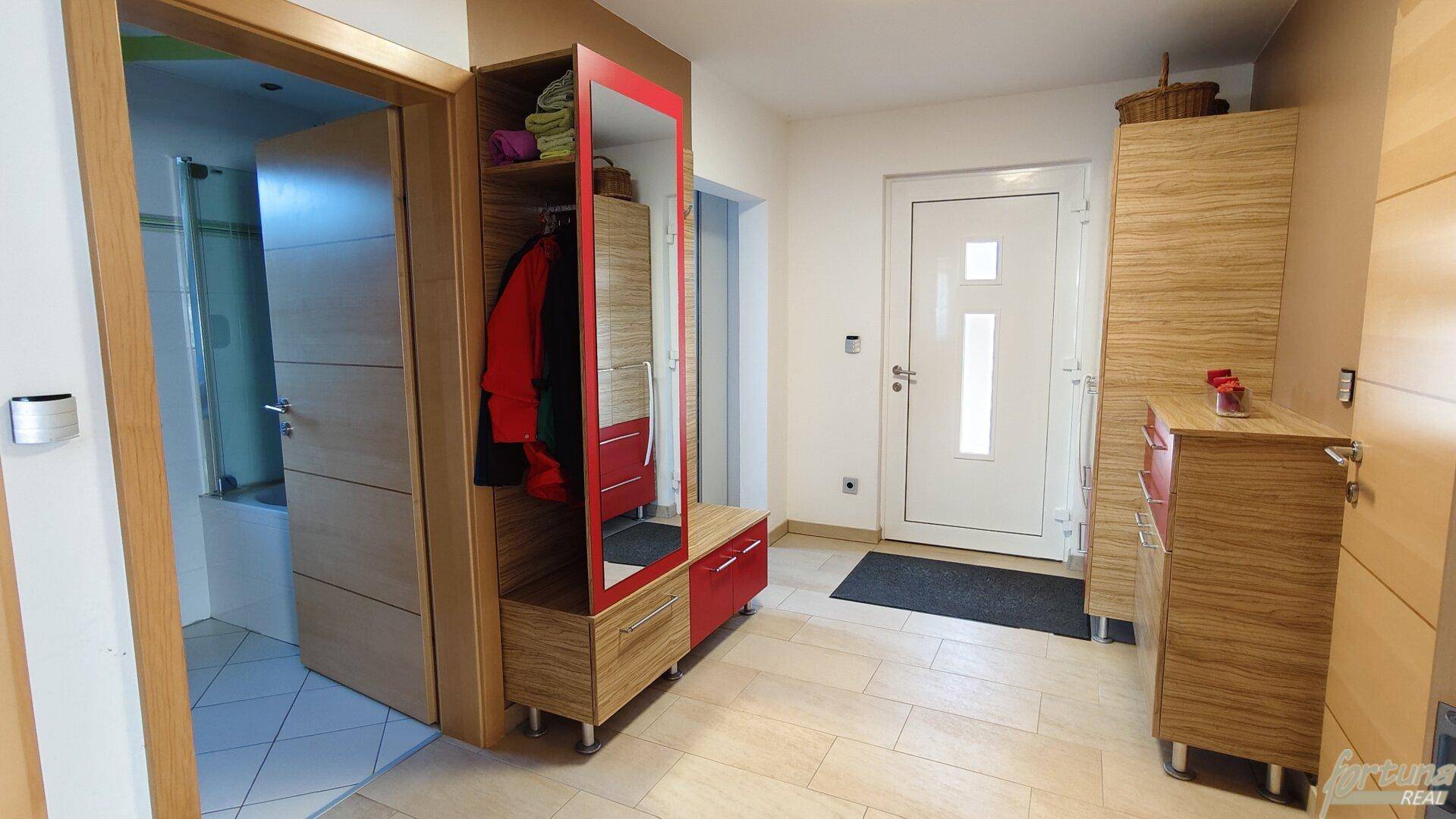 Heller Eingangsbereich mit Holzmöbeln, Garderobe und weißer Eingangstür.