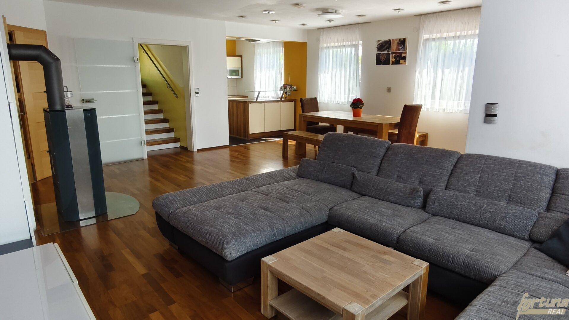 Gemütlicher Wohnbereich mit großem Ecksofa, Holzboden und Kaminofen.