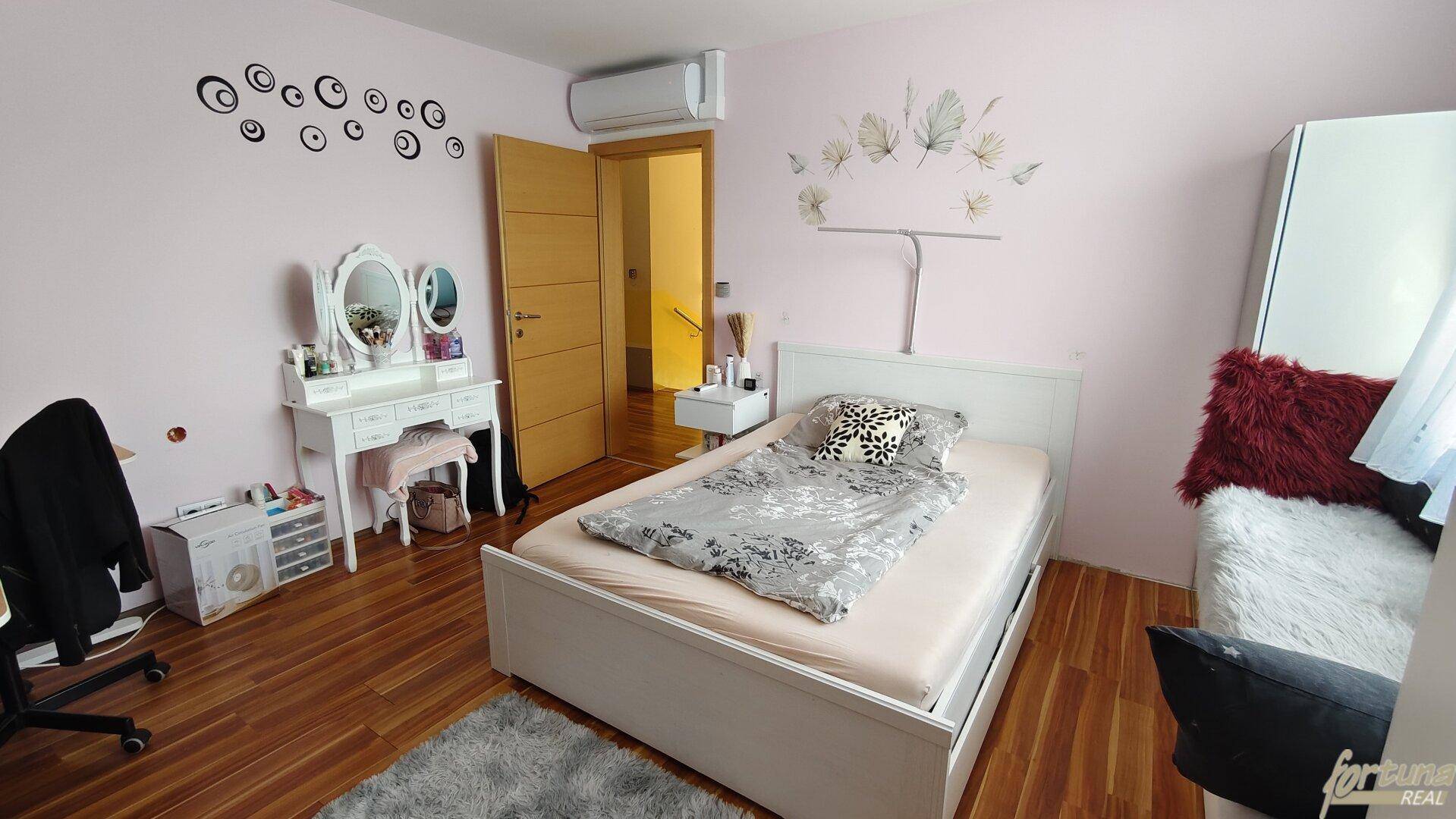 Helles Schlafzimmer mit Doppelbett, Schminktisch und rosa Wänden.