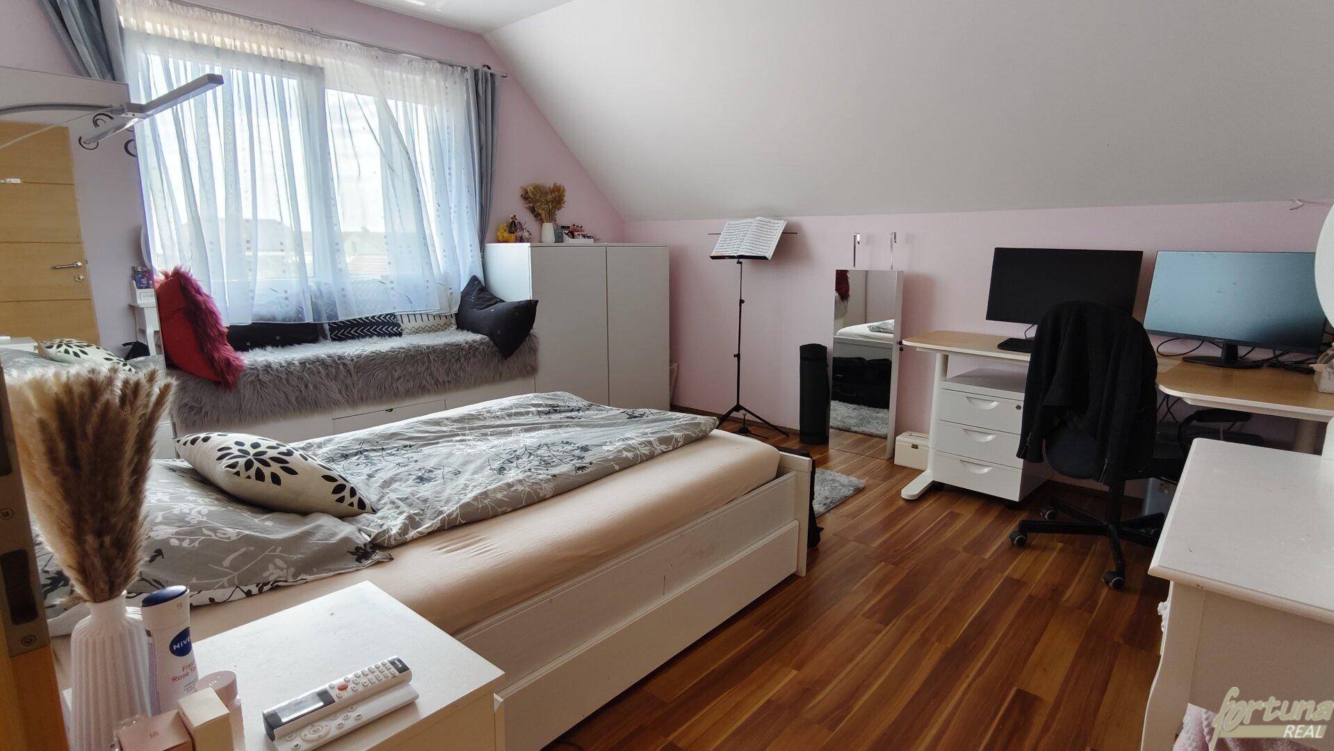 Geräumiges Schlafzimmer im Dachgeschoss mit Bett, Schreibtisch und großen Fenstern.