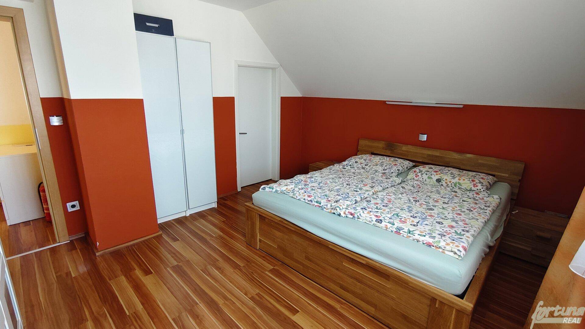 Schlafzimmer mit Holzbett, weißem Kleiderschrank und farbigen Akzentwänden.