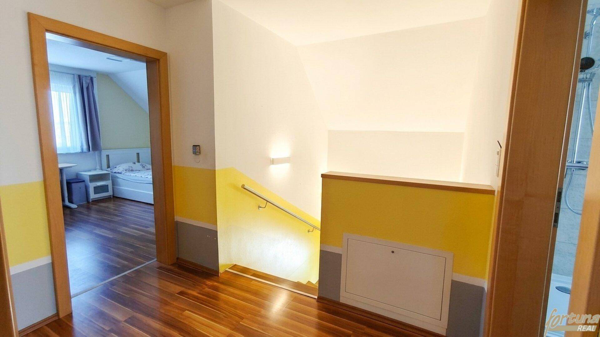 Flur mit Holztreppe und Zugang zu einem Schlafzimmer, gestaltet mit farbigen Wänden.