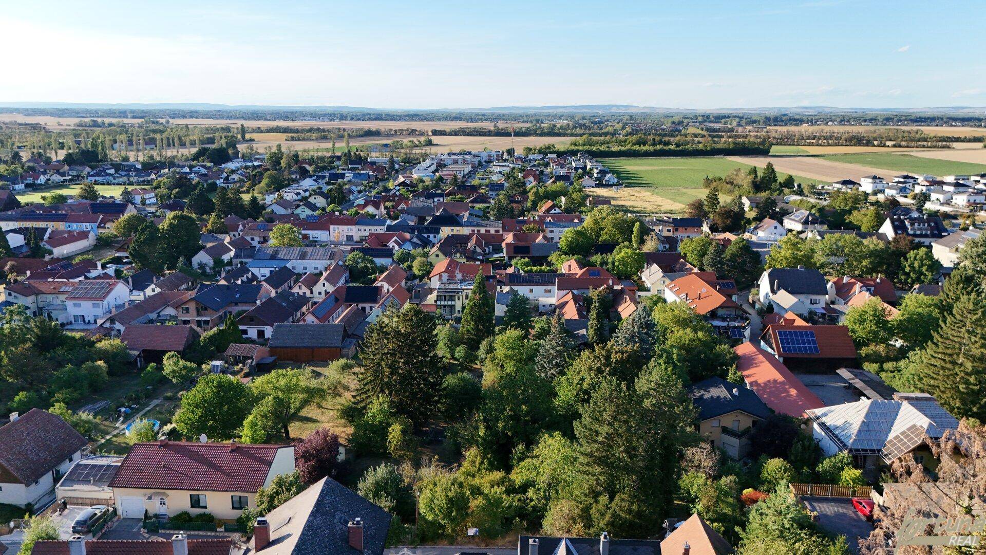 Panoramablick aus der Vogelperspektive auf eine ländliche Gemeinde mit weiten Feldern im Hintergrund unter blauem Himmel.