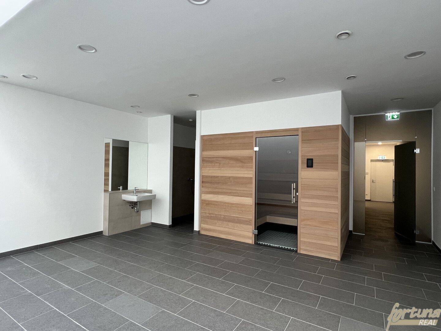 Gemeinschaftlicher Wellnessbereich mit Sauna, Waschbecken und großformatigen Fliesen.