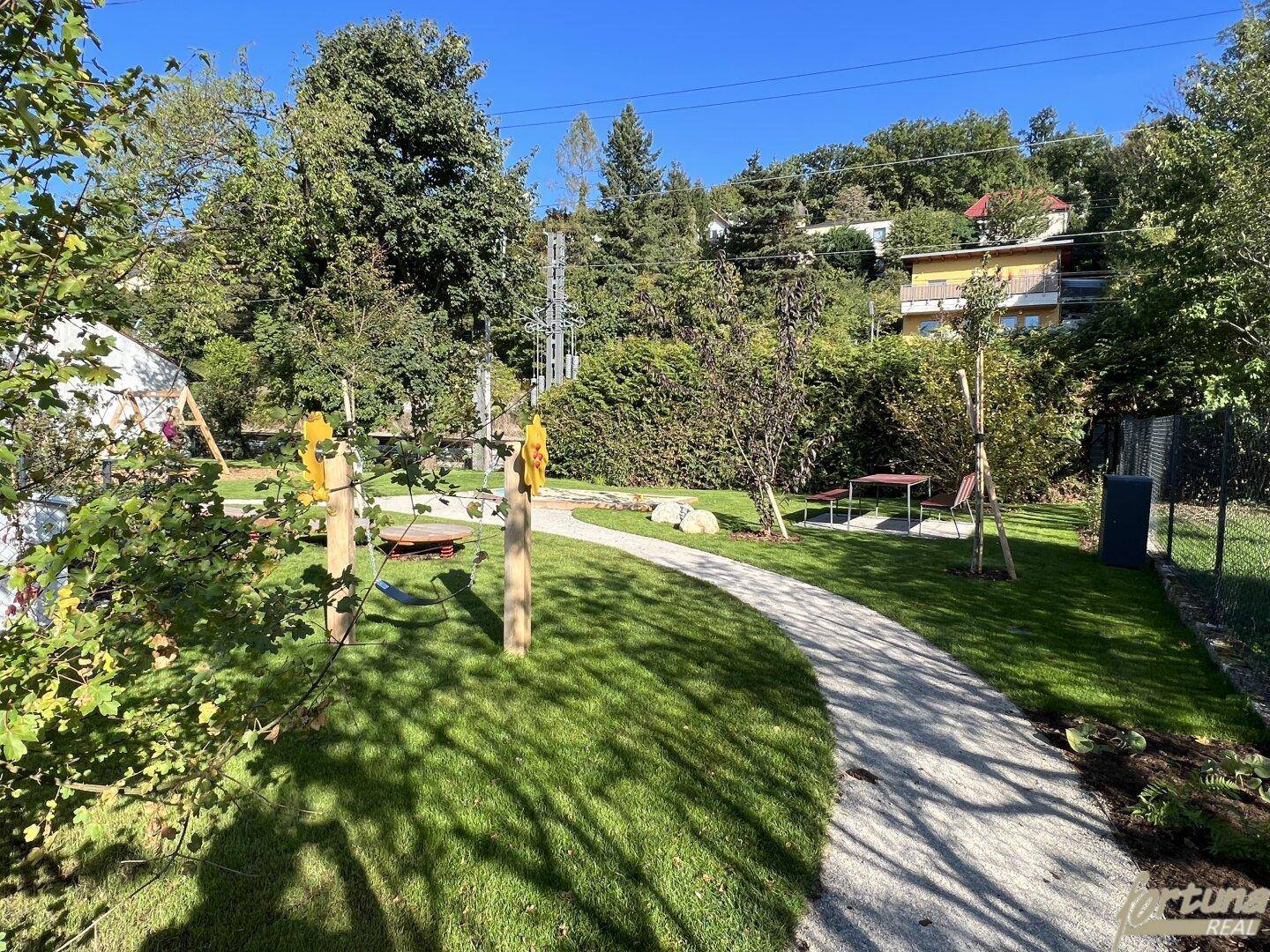 Gemeinschaftlicher Gartenbereich mit Spielplatz, Rasenfläche und Wegen für Erholung.