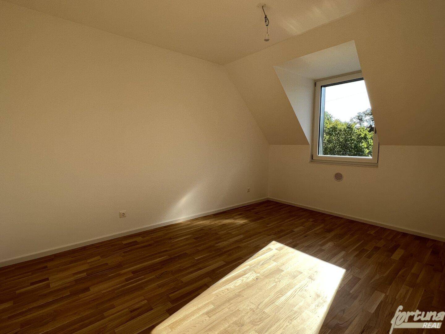 Geräumiges Zimmer mit Holzboden, Dachschräge und Fenster, ideal als Schlaf- oder Arbeitszimmer.