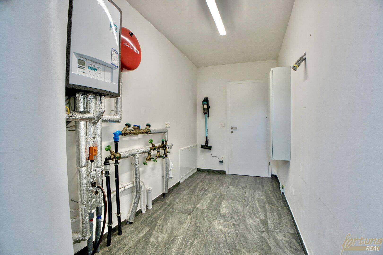Funktionaler Hauswirtschaftsraum mit Heizungsanlage, Leitungen und Fliesenboden.