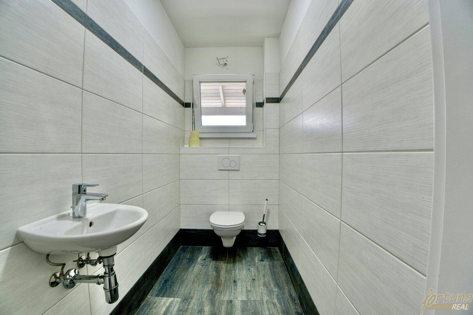 Modernes Gäste-WC mit Wand-WC, kleinem Waschbecken und zweifarbigen Fliesen.