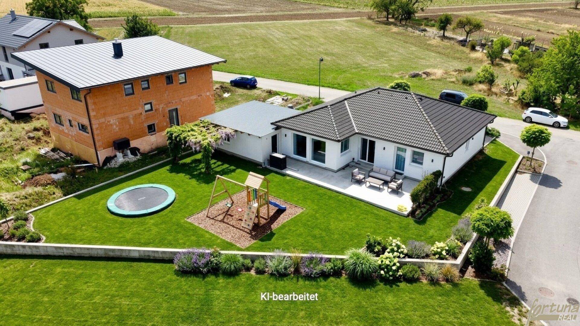 Gepflegter Gartenbereich mit Rasenfläche, Terrasse, Trampolin und Spielplatz neben dem modernen Haus.