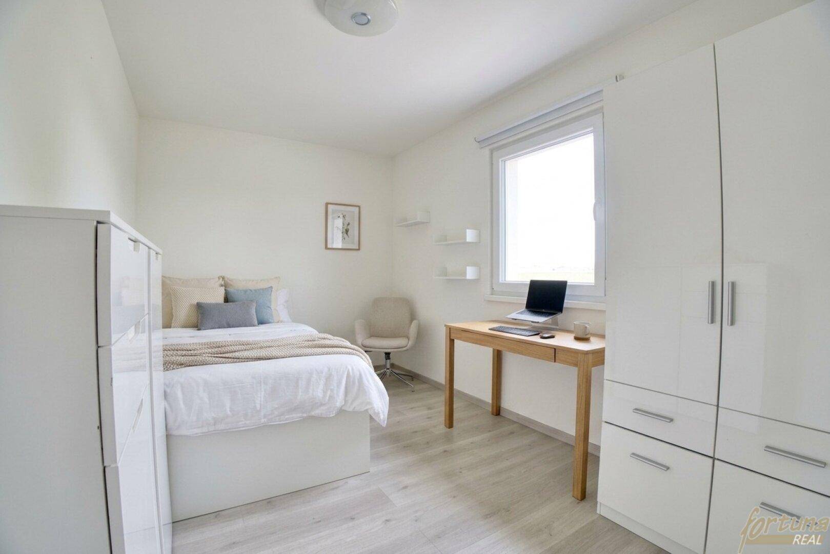 Helles Schlafzimmer mit modernem Laminatboden, weißem Kleiderschrank und Schreibtisch am Fenster.