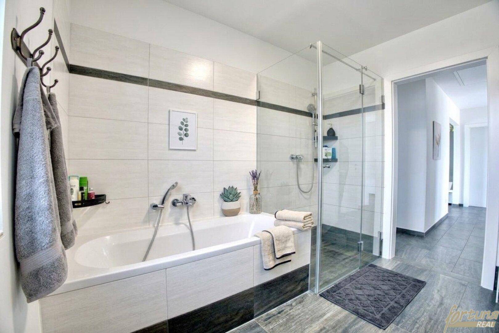 Helles Badezimmer mit Badewanne, Glasduschkabine und modernen Fliesen in Grau und Weiß.