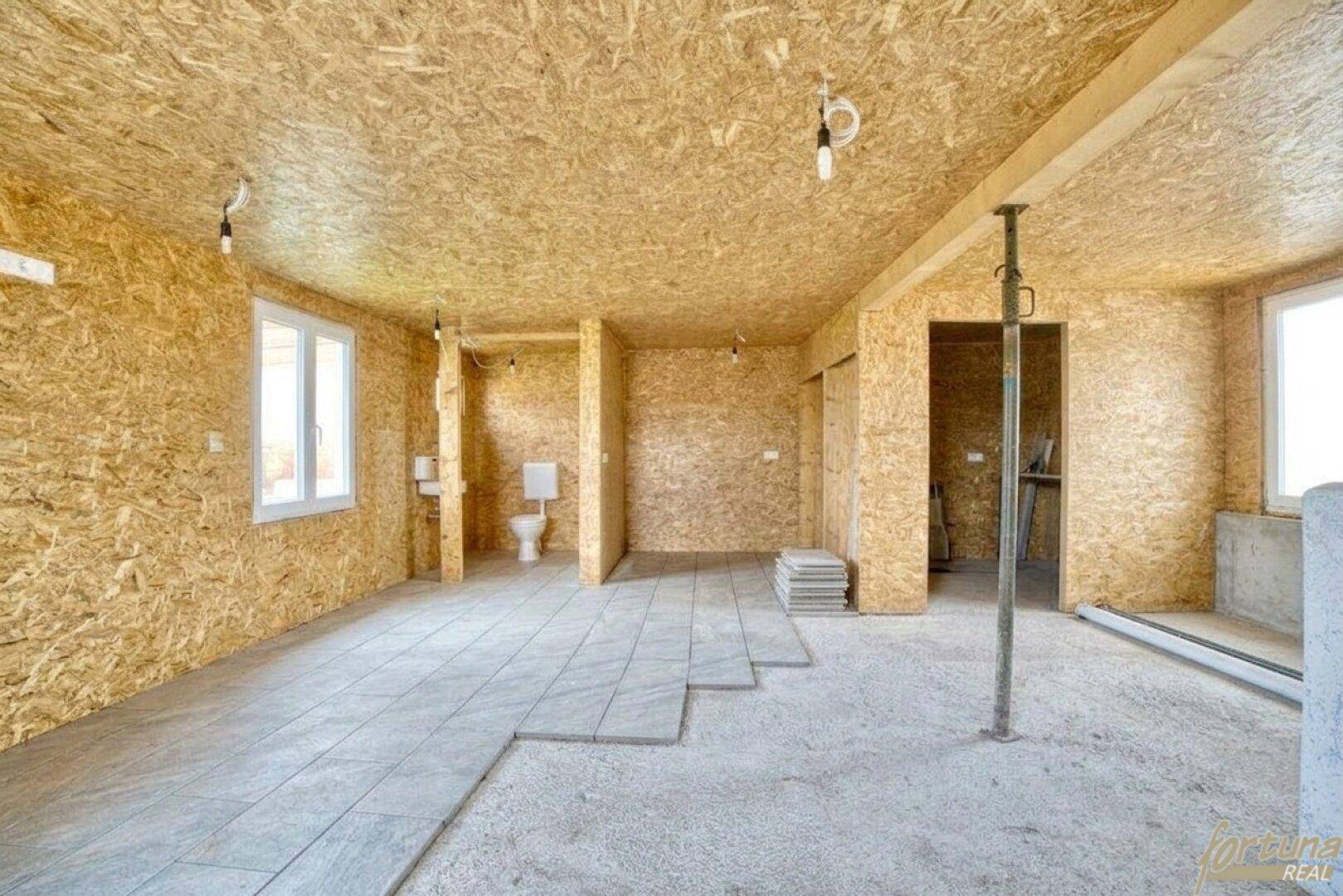 Rohbau eines Raumes mit OSB-Plattenwänden, teilweise gefliestem Boden und sichtbaren Installationen.