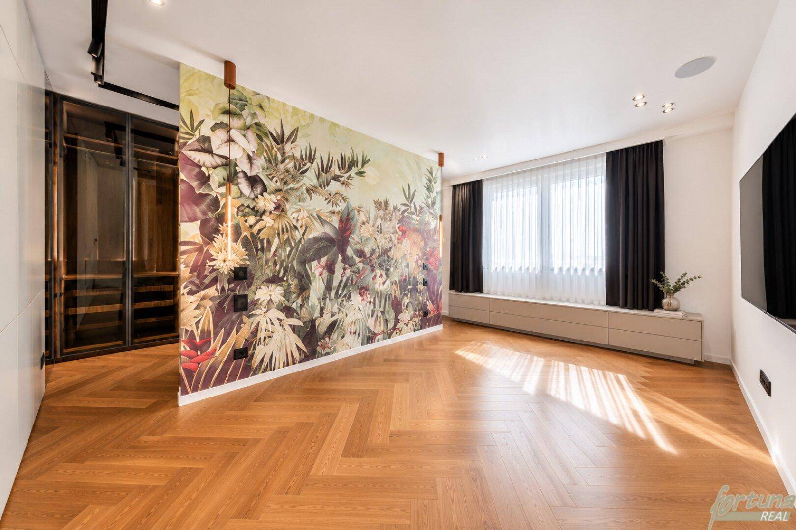 Geräumiges Schlafzimmer mit auffälliger Blumentapete, Fischgrätparkett und integriertem begehbarem Kleiderschrank.