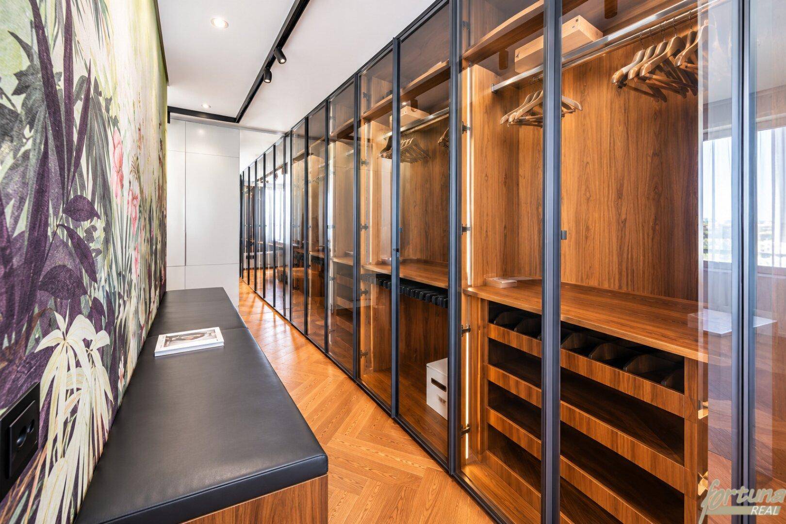 Eleganter begehbarer Kleiderschrank mit Glasfronten und Holzinterieur, perfekt organisiert.