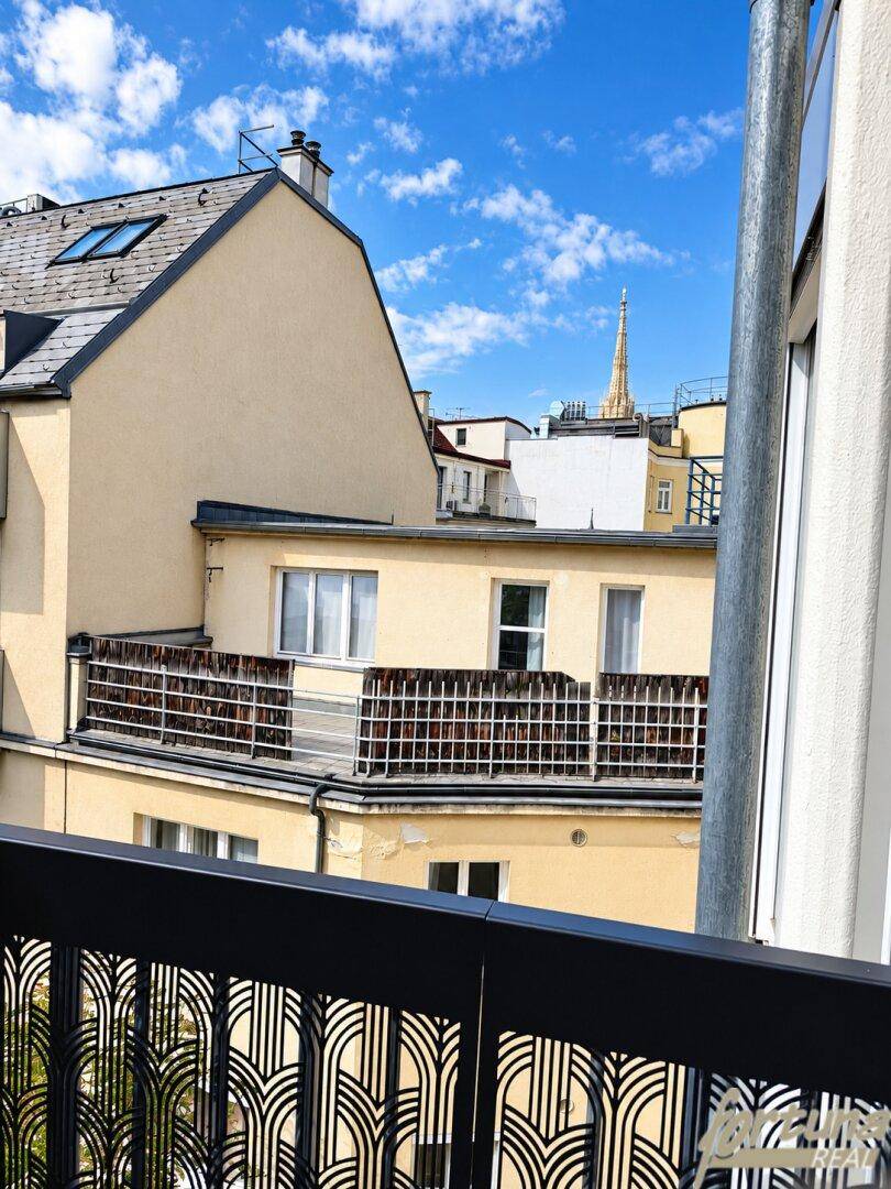 Blick vom Balkon auf die umliegenden Gebäude und einen Kirchturm unter blauem Himmel.