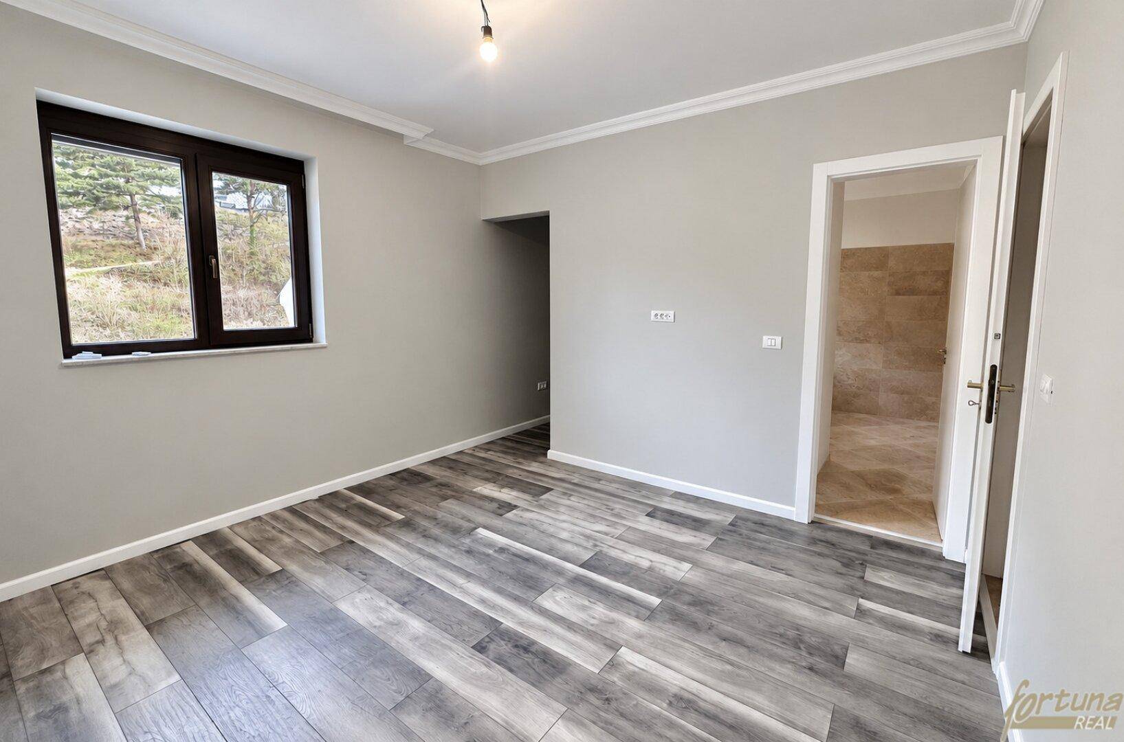 Leeres Schlafzimmer mit modernem Holzboden und direktem Zugang zu einem Badezimmer.
