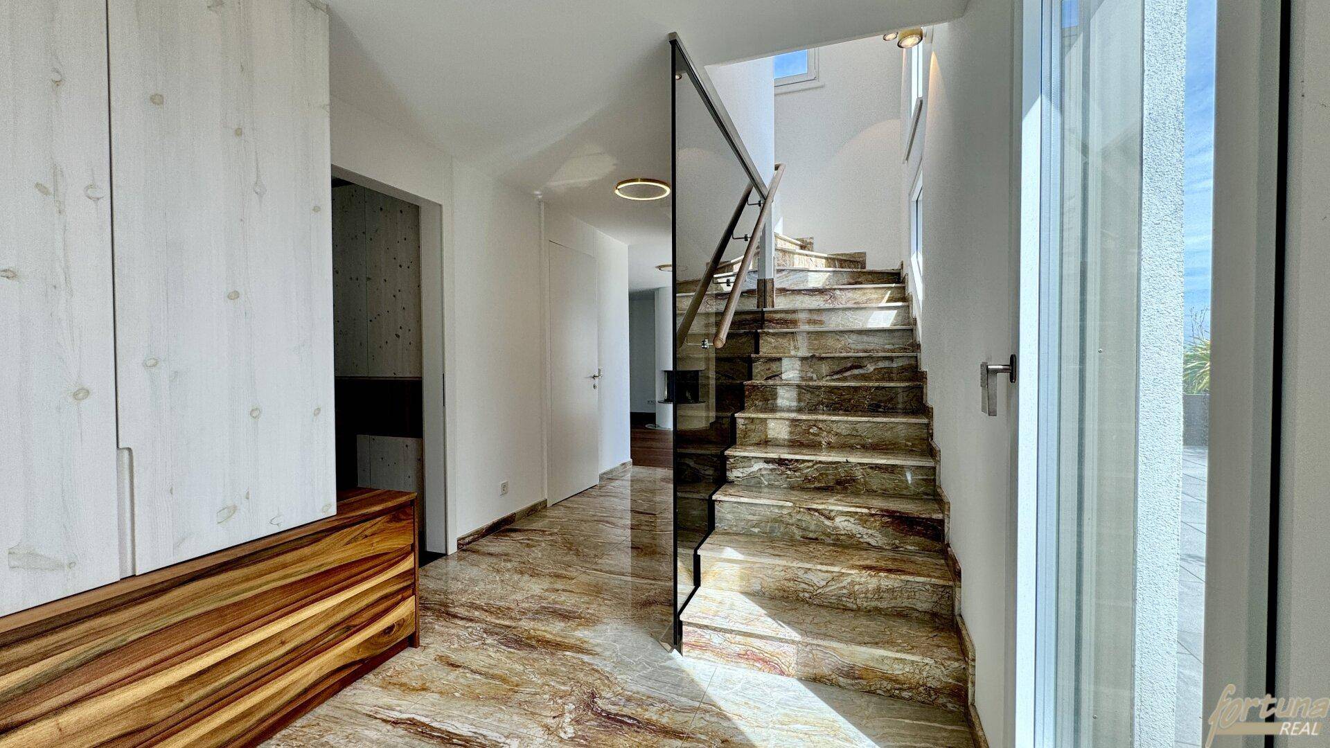 Heller Flur mit Marmorboden und moderner Glasbrüstung an der Treppe, die nach oben führt.
