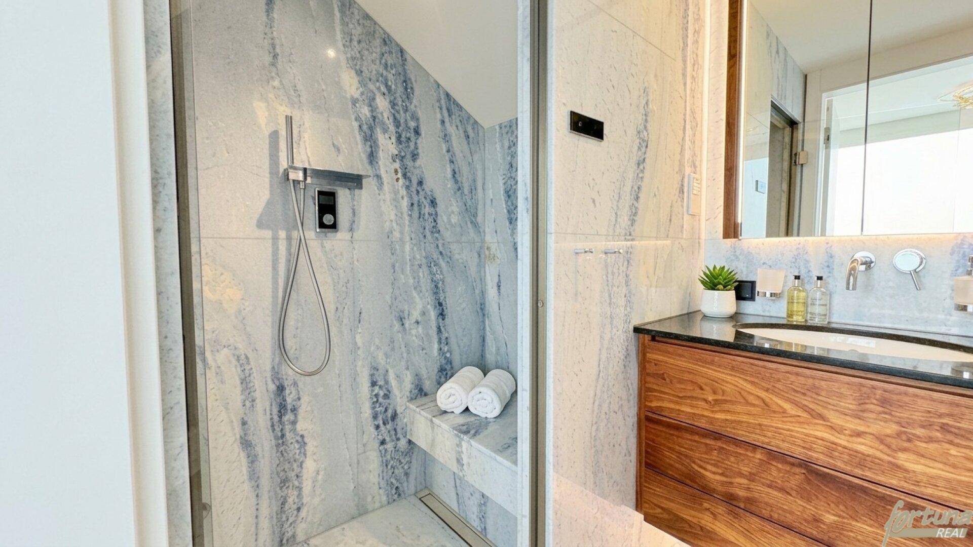 Elegantes Badezimmer mit blauen Marmorfliesen, begehbarer Dusche und modernem Waschtisch.