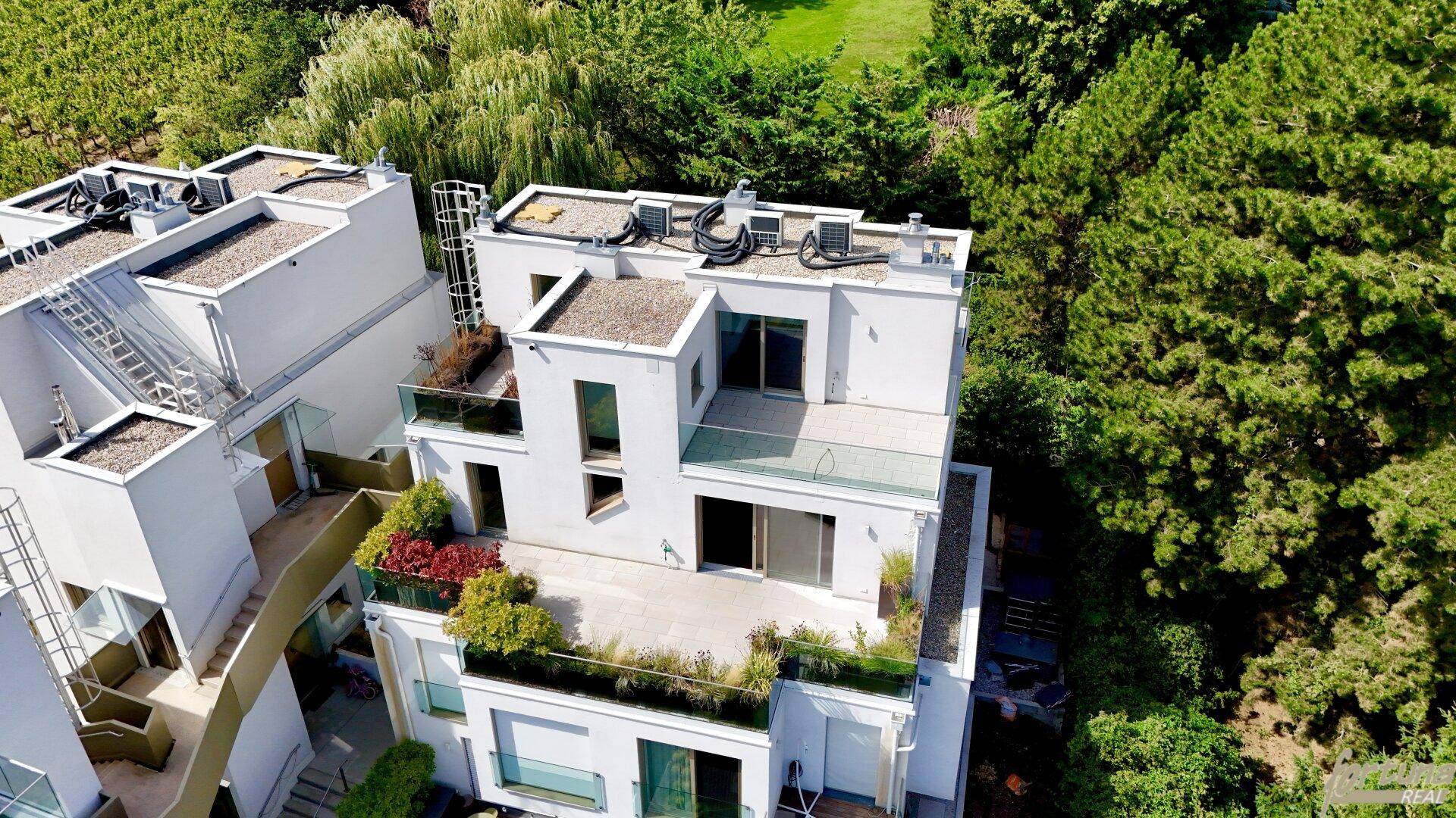 Moderne Architektur mit mehreren Terrassen und Flachdächern, umgeben von üppiger Vegetation.