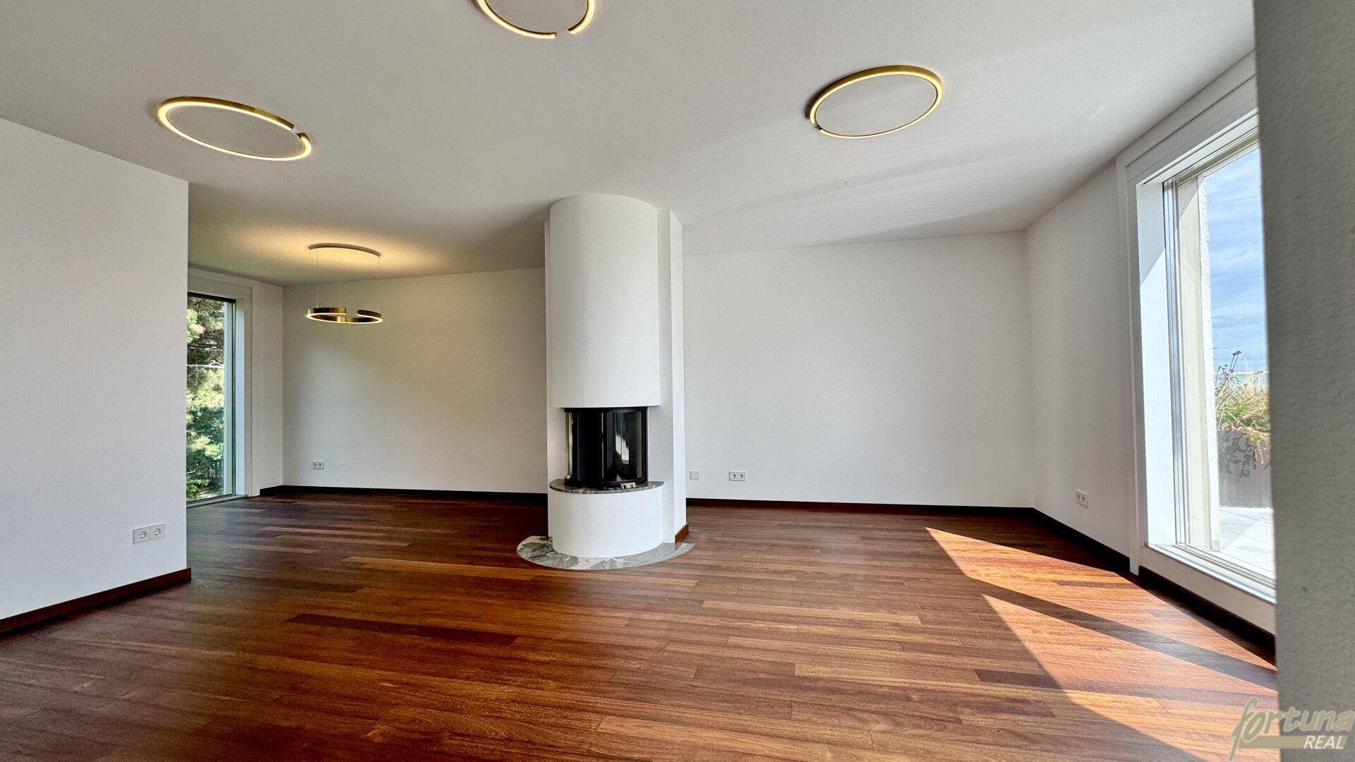 Geräumiges Wohnzimmer mit Holzboden, modernem Kamin und großen Fenstern für viel Tageslicht.