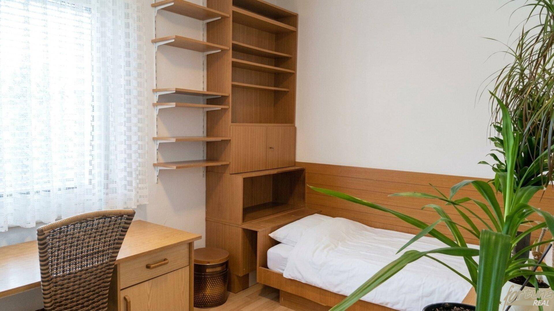 Helles Schlafzimmer mit Einzelbett, Holzregal und Schreibtisch am Fenster.