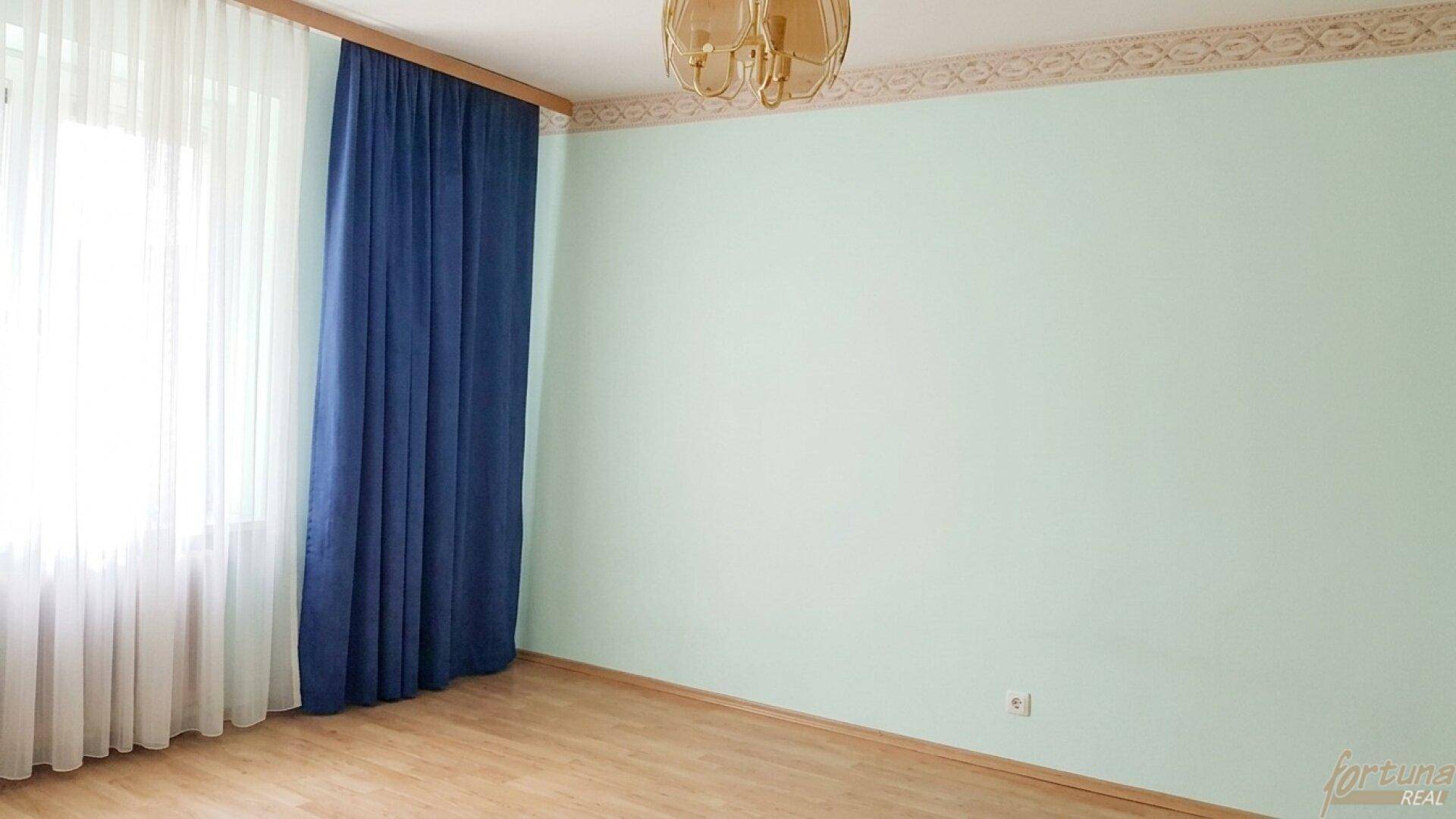 Helles Zimmer mit Parkettboden, hellgrünen Wänden und blauen Vorhängen.
